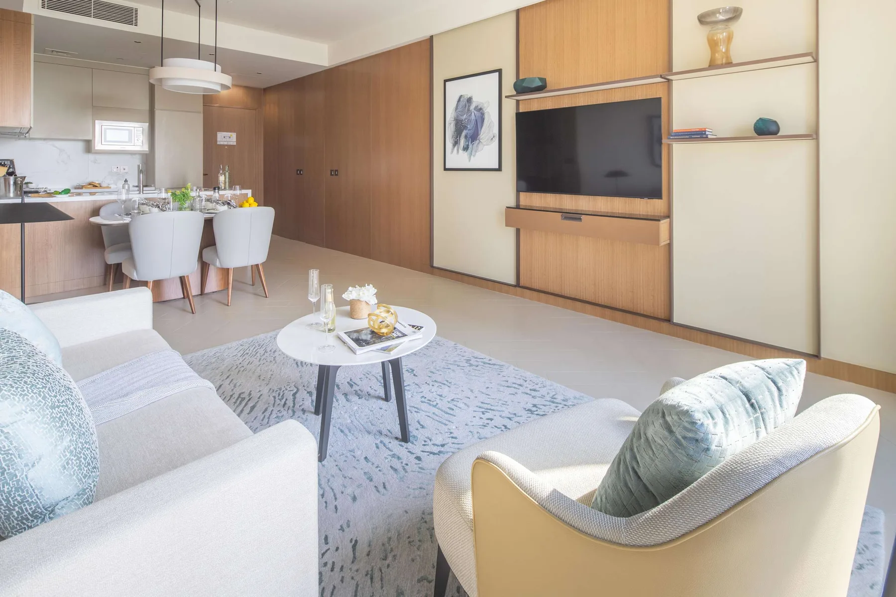 A bright living and dining area with seating, a table, and a wall-mounted television.