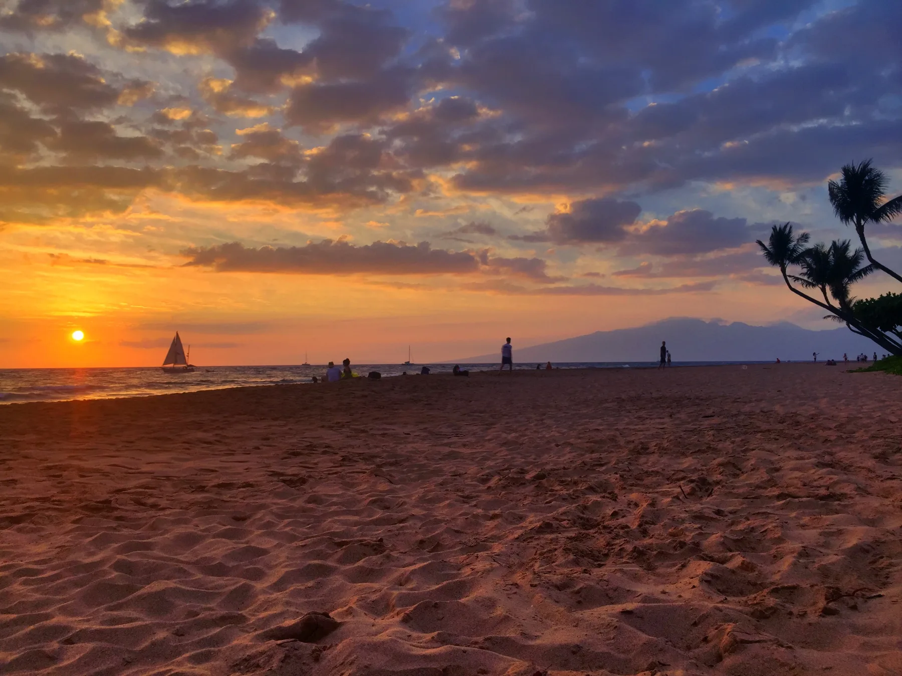 Una playa de arena al atardecer, con un velero en el horizonte.