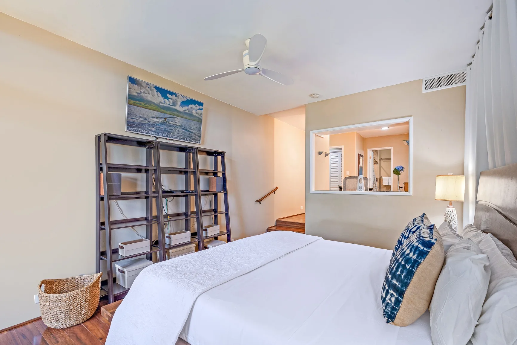 Un dormitorio con una cama blanca y estanterías abiertas junto a la pared.