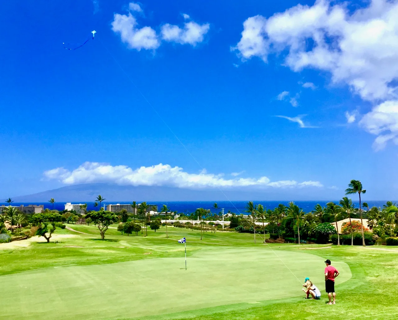 Un campo de golf se extiende hacia el océano bajo un cielo azul.