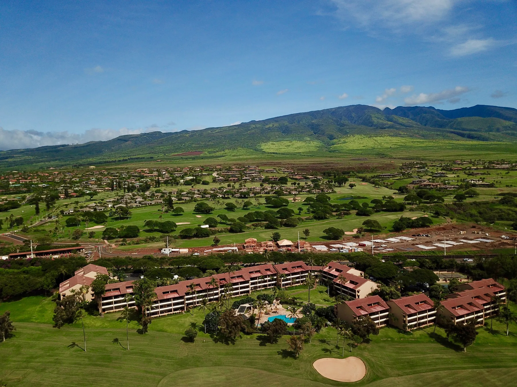 Vista aérea de una zona residencial con campos verdes y montañas a lo lejos.