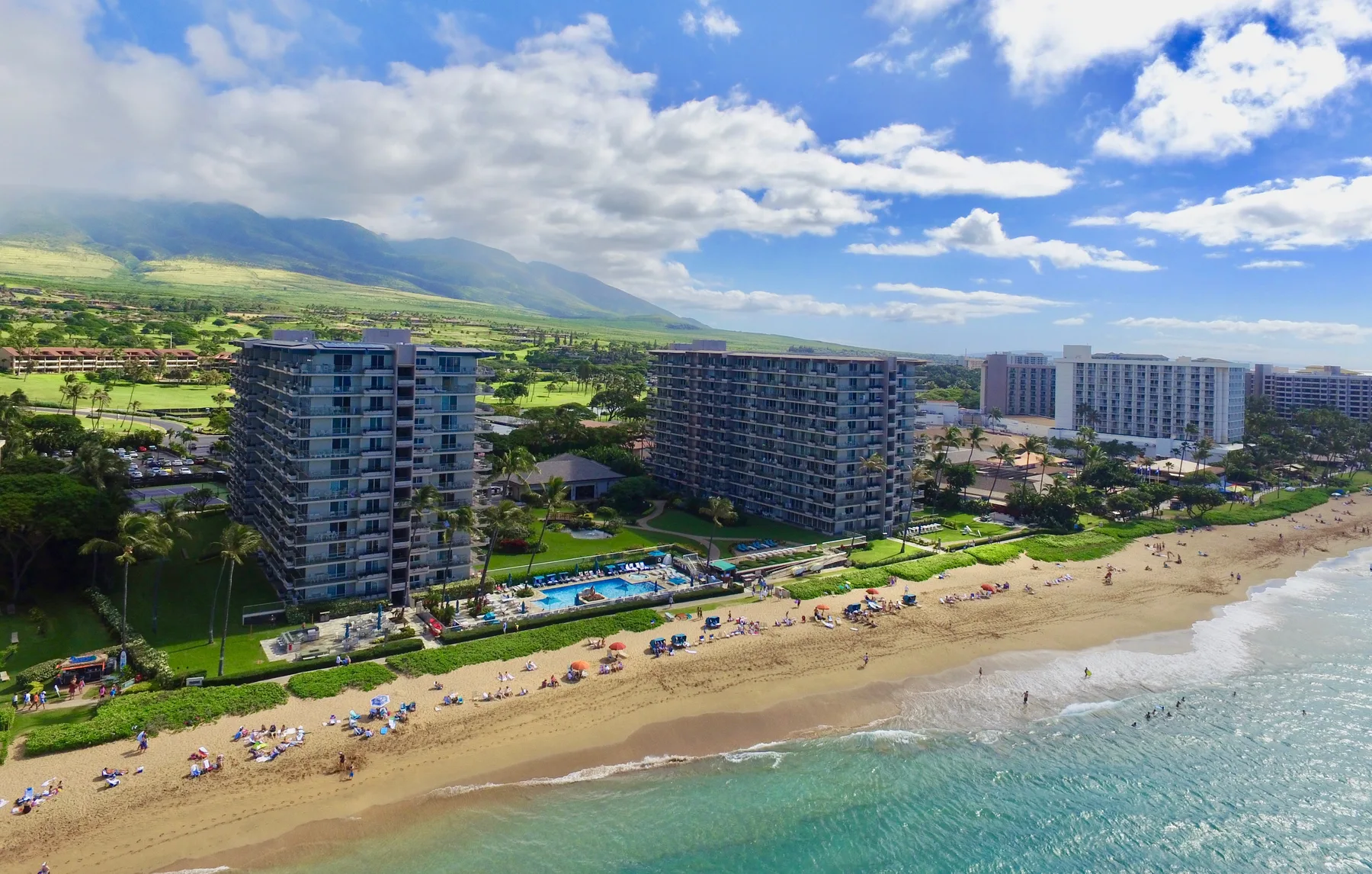 Vista aérea de una playa con edificios turísticos, costa arenosa y olas del océano.