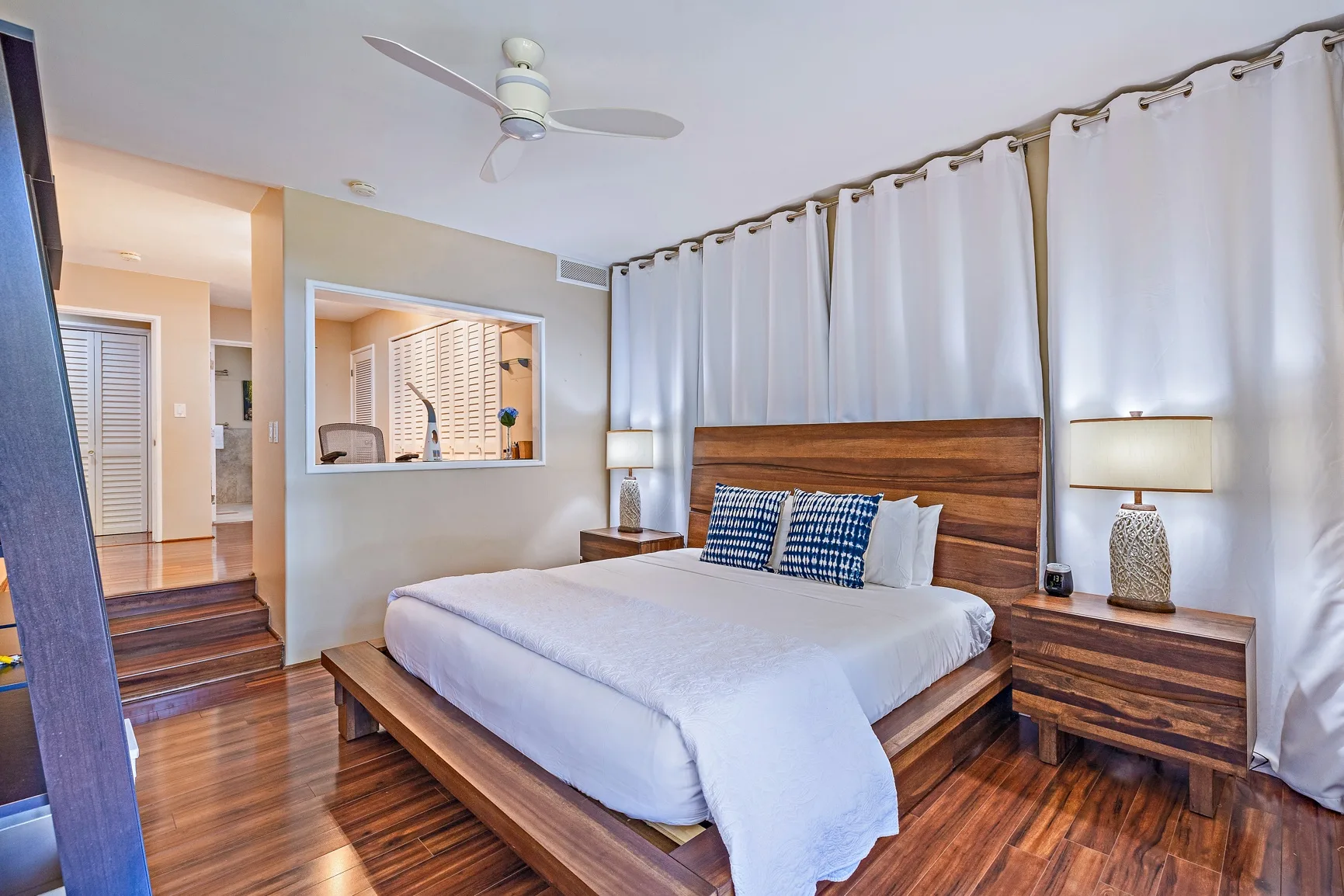 Un dormitorio con una cama de madera, almohadas azules y cortinas blancas.