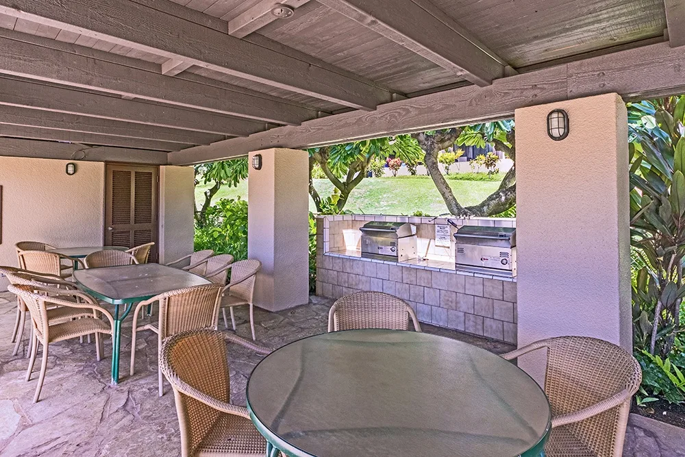 Comedor exterior cubierto con mesas y una barra de barbacoa empotrada.