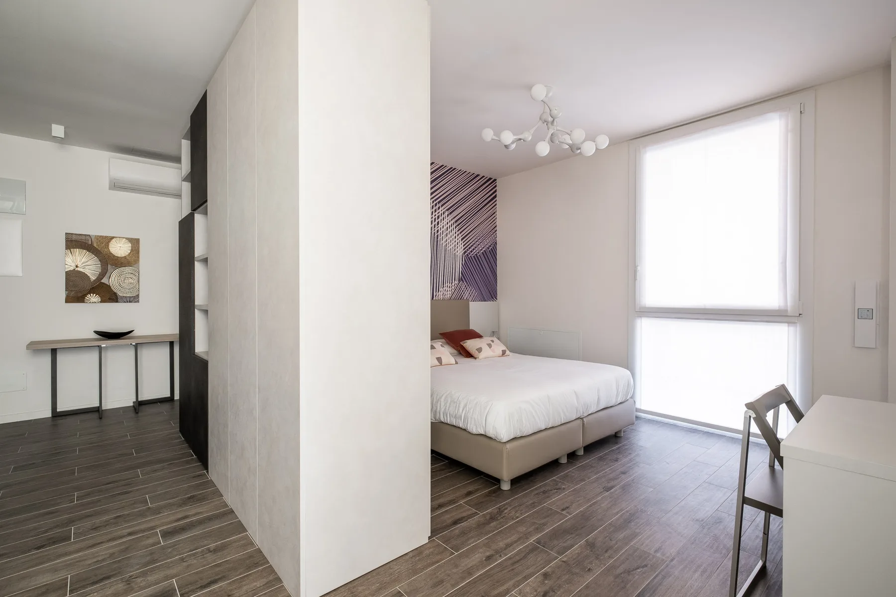 A bright bedroom with a bed beside a large window and a desk.
