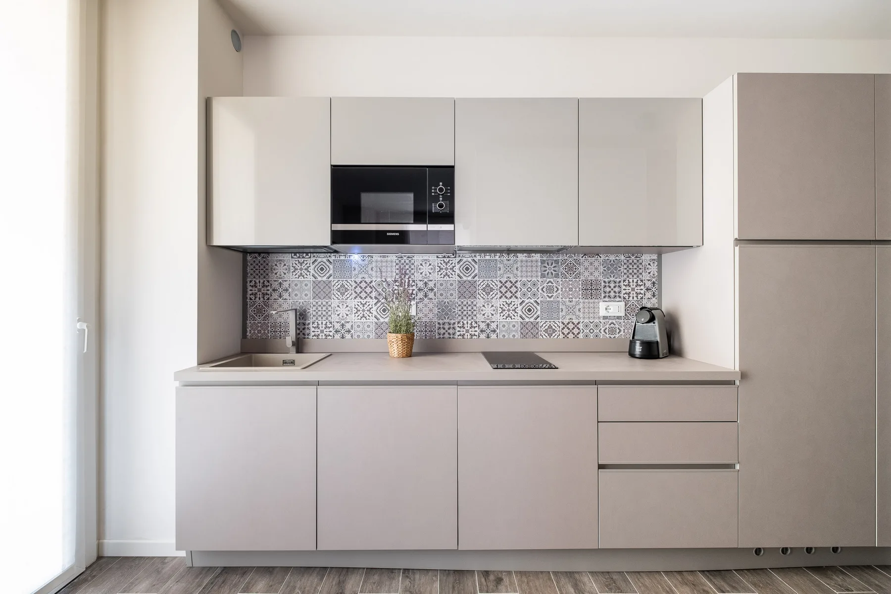 A modern kitchen with pale cabinets and a patterned backsplash.