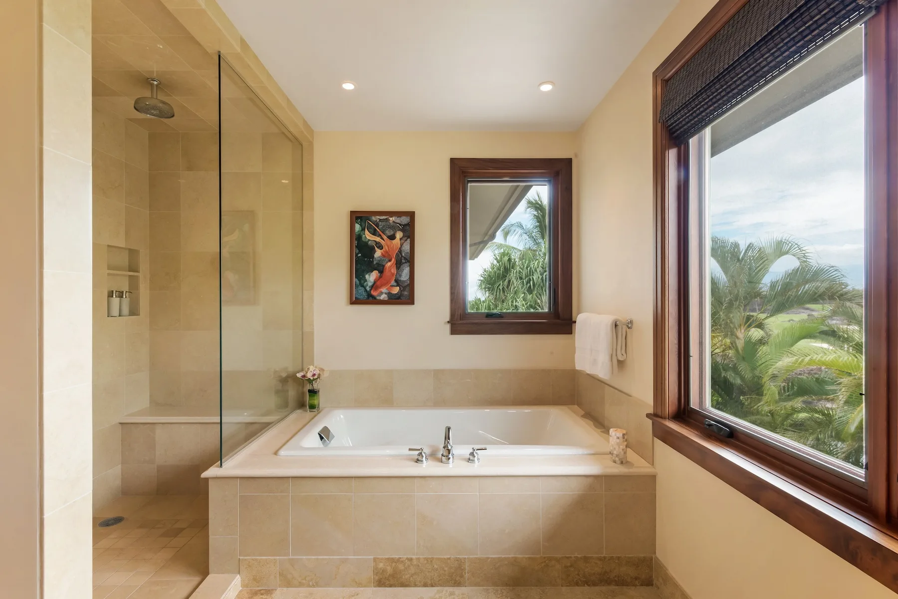 Un baño con bañera, ducha de vidrio y ventanas con vistas a la vegetación.