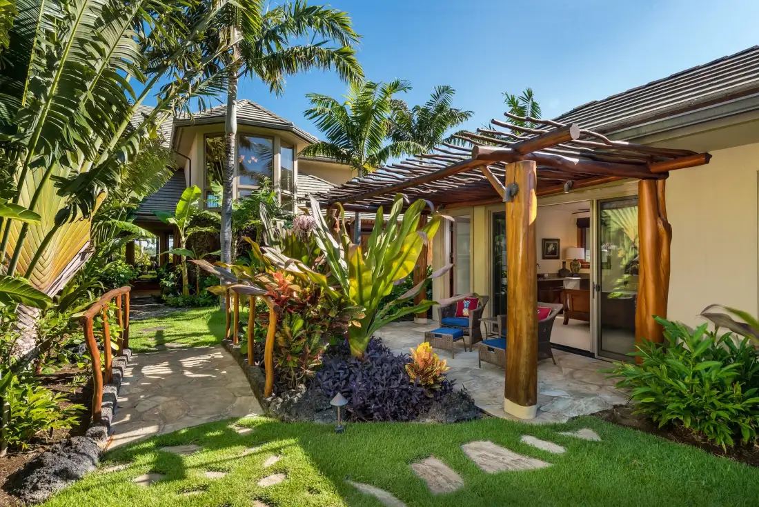 Una casa tropical se abre a un patio ajardinado con una pérgola de madera.