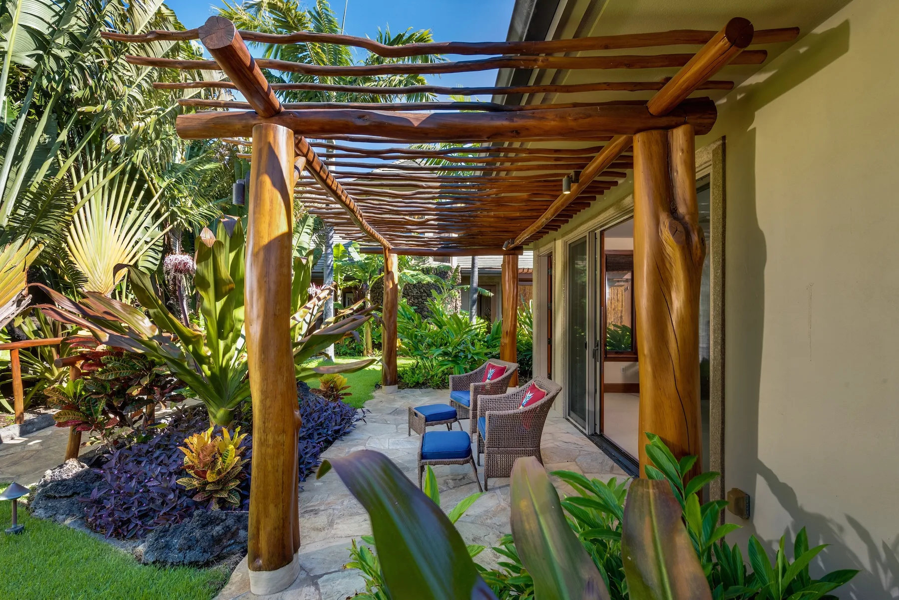 Un patio cubierto con asientos da a un exuberante jardín tropical.