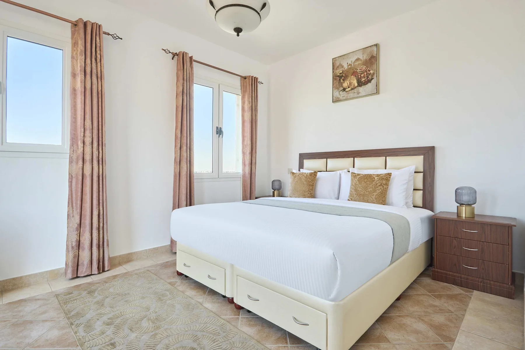Un dormitorio luminoso cuenta con una cama tendida y ventanas con cortinas.