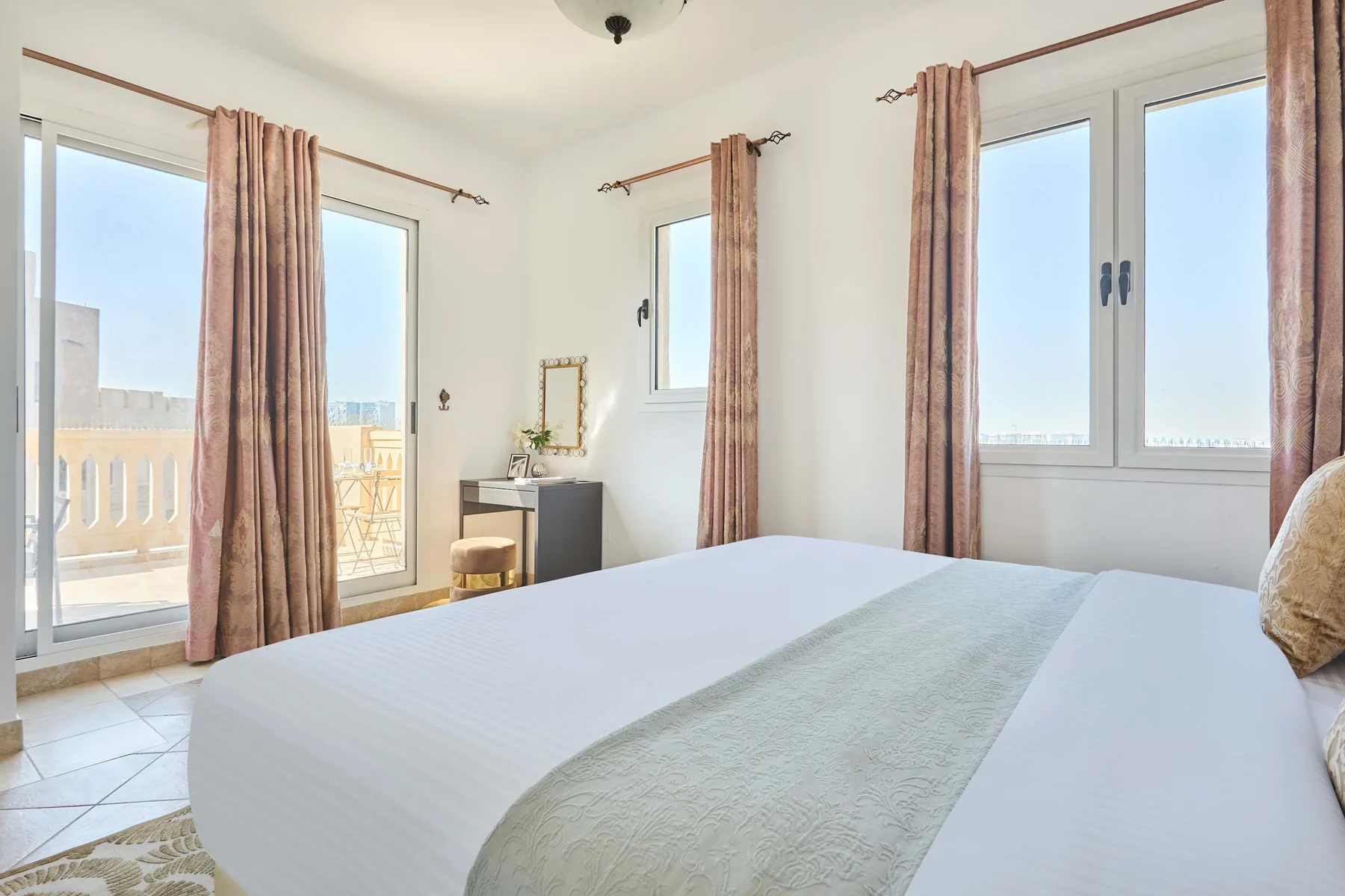 Un dormitorio luminoso con una cama tendida y ventanas altas.