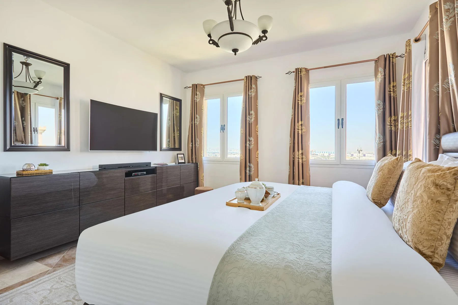 Dormitorio con una cama bien tendida, un televisor y ventanas con cortinas.
