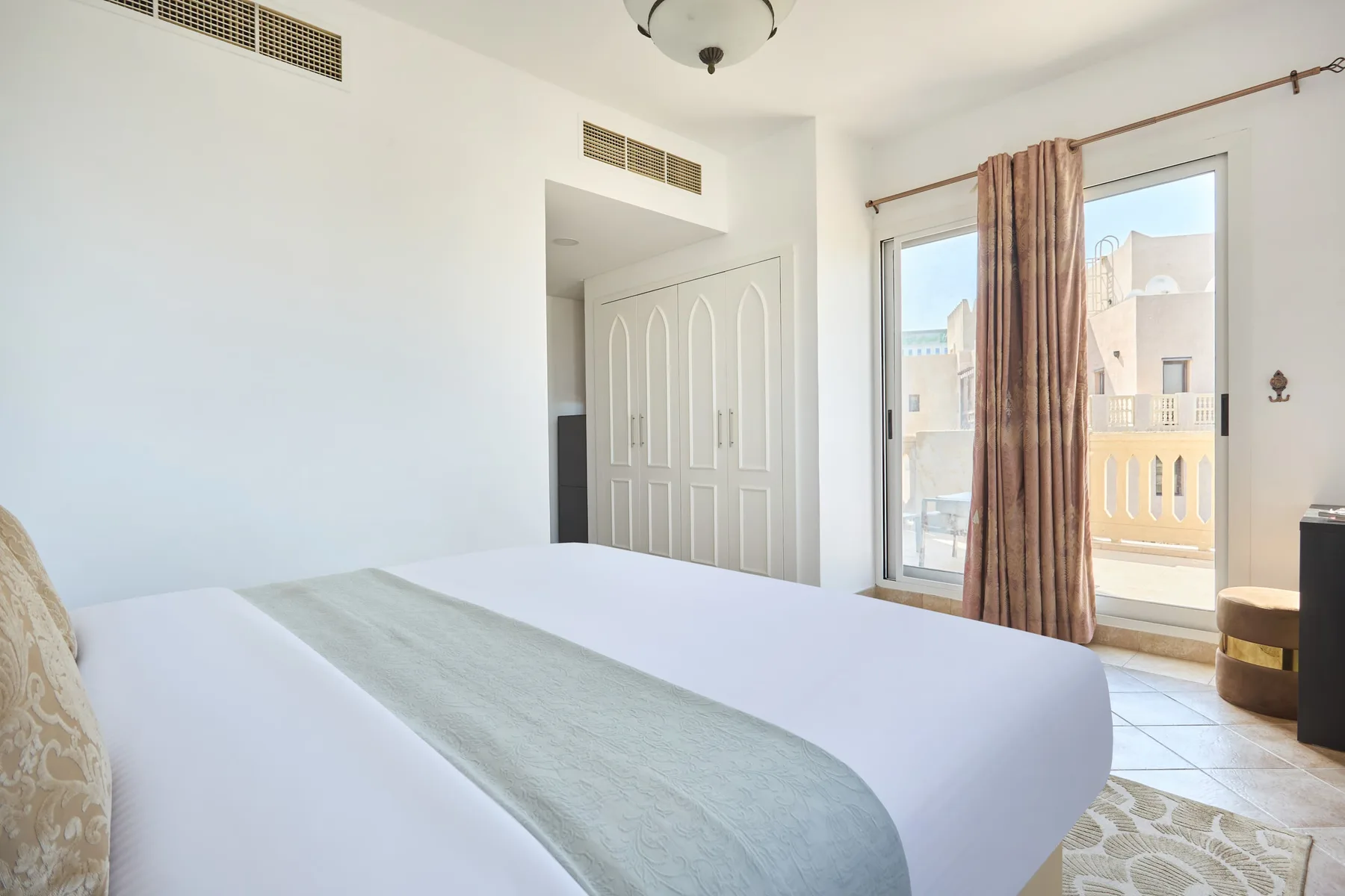 Un dormitorio luminoso con una cama bien tendida y grandes puertas de vidrio hacia un balcón.