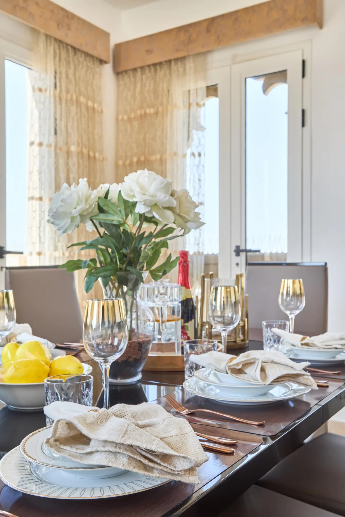 Una mesa de comedor está preparada con platos, copas, servilletas dobladas y flores.