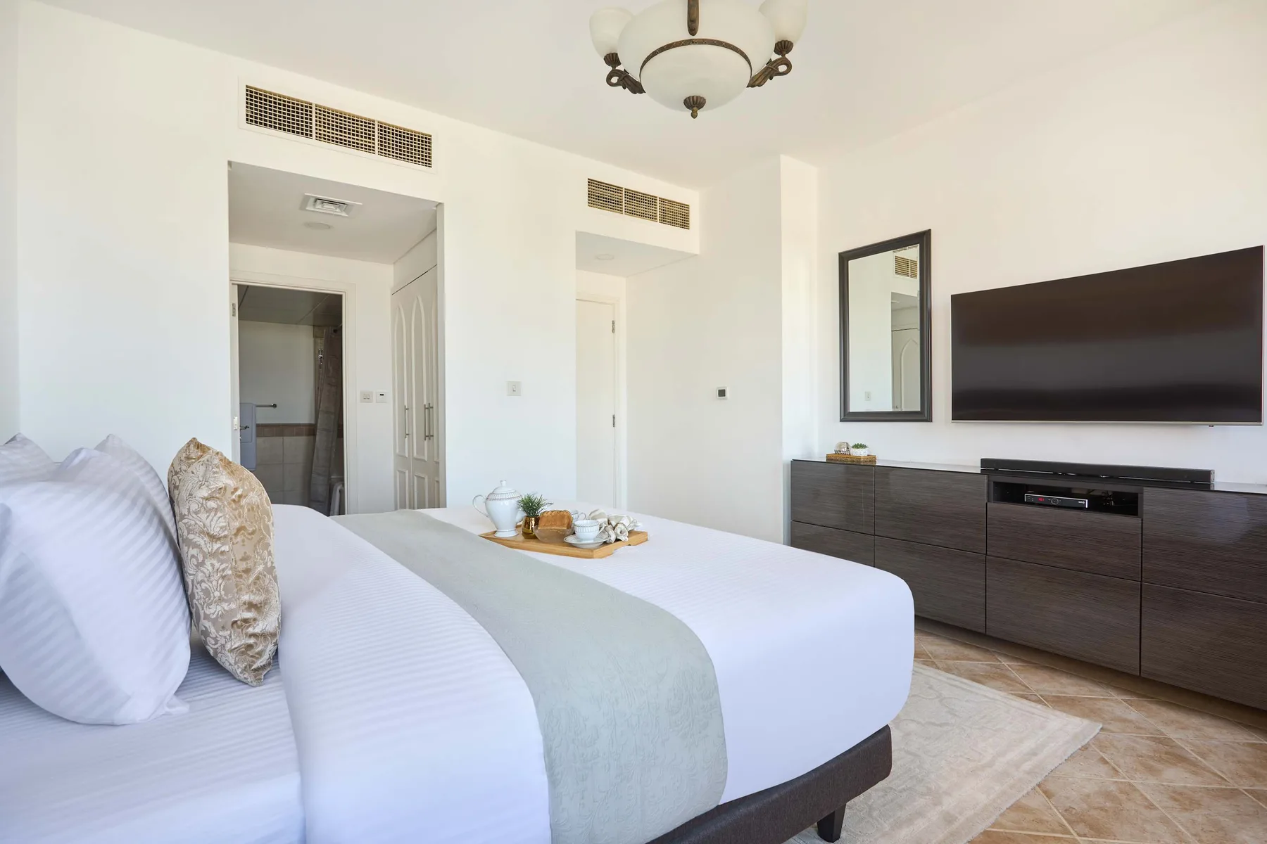 Un dormitorio luminoso con una cama tendida y un televisor sobre un mueble bajo.
