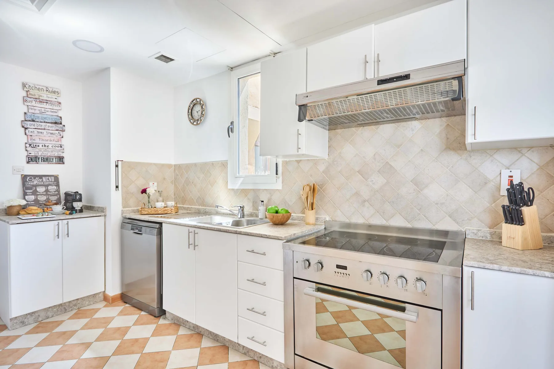 Una cocina luminosa con gabinetes blancos, un salpicadero de azulejos y una estufa de acero inoxidable.