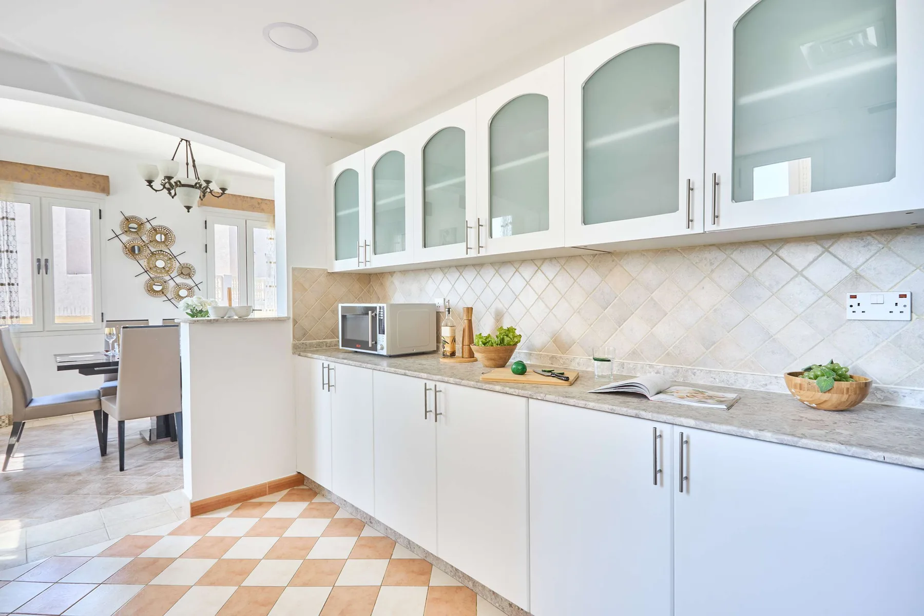 Una cocina luminosa con gabinetes blancos, una encimera y un comedor contiguo.