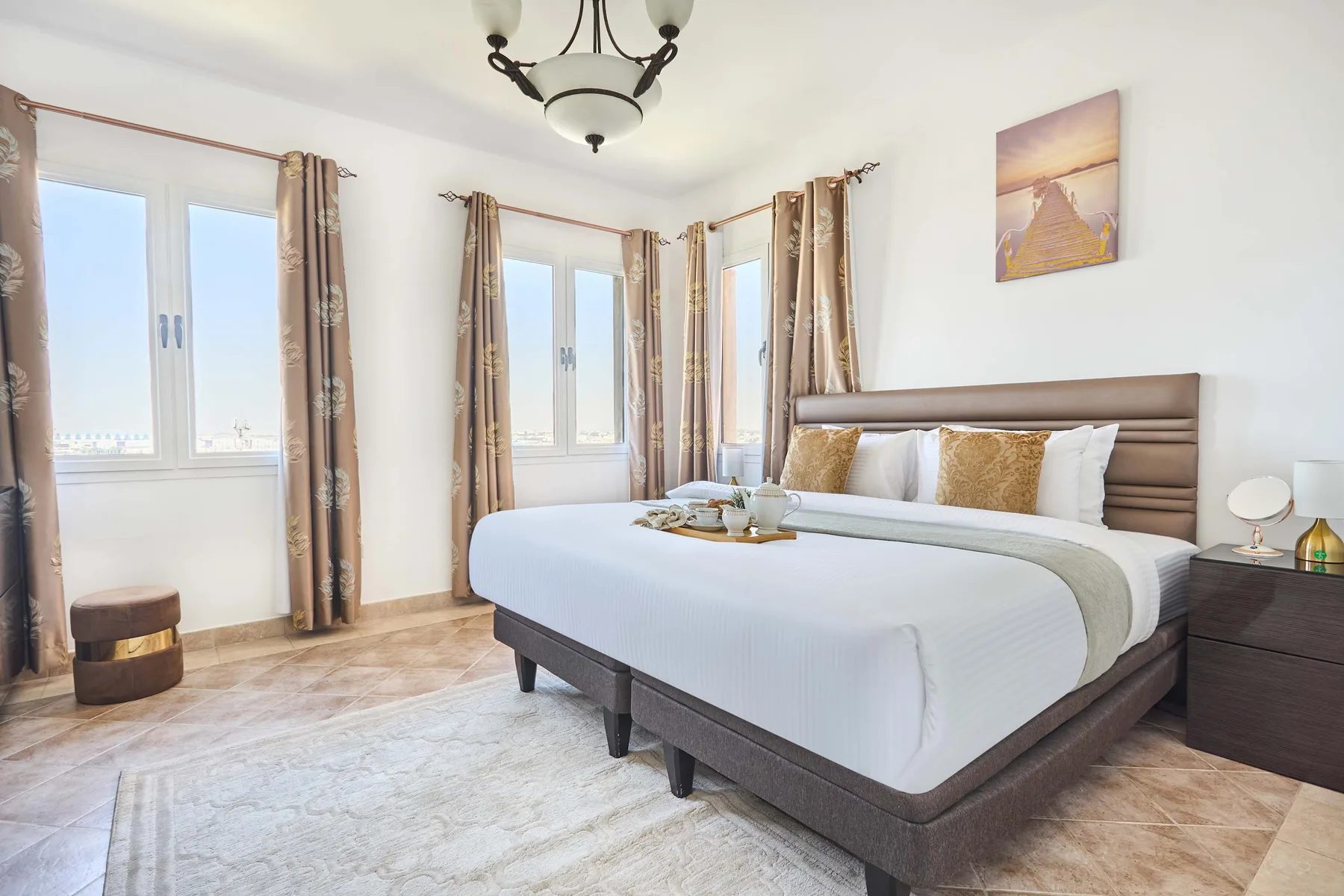 Un dormitorio luminoso con una cama bien arreglada y ventanas altas con cortinas.
