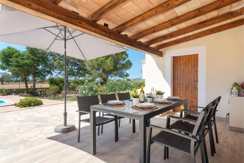 A covered outdoor dining area with a table and chairs beside a garden.