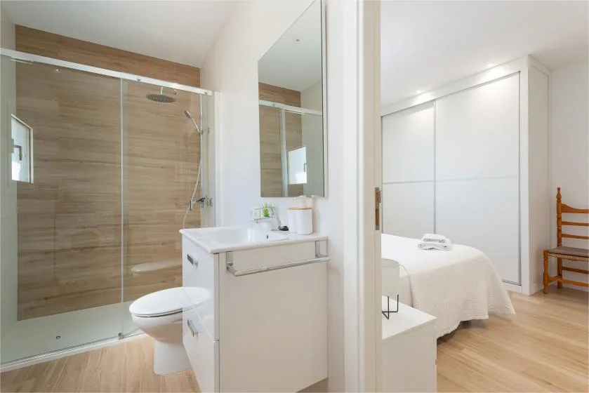 A bathroom with a glass shower and sink opens onto a bedroom.