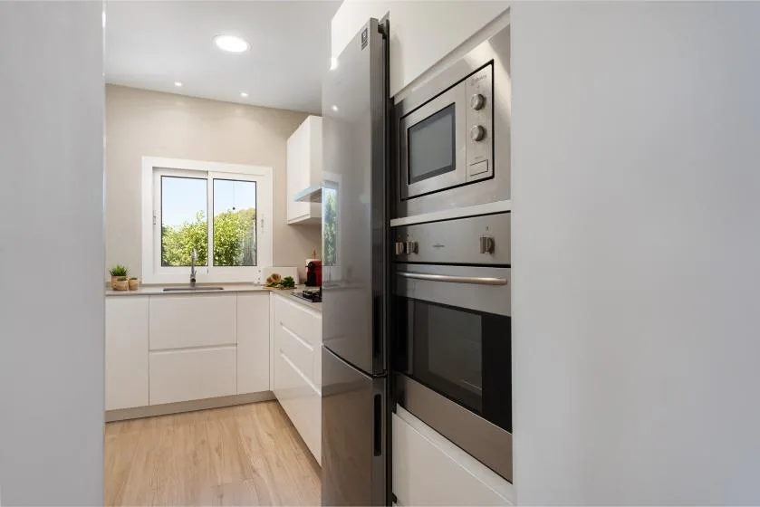 A bright modern kitchen with white cabinets, a window, and built-in appliances.