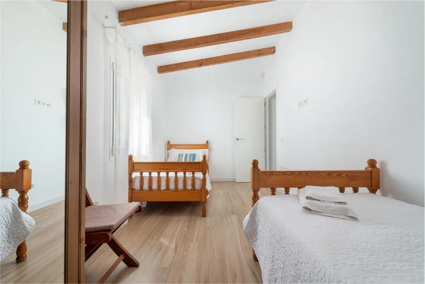 A bright bedroom with wooden beds, white bedding, and exposed ceiling beams.