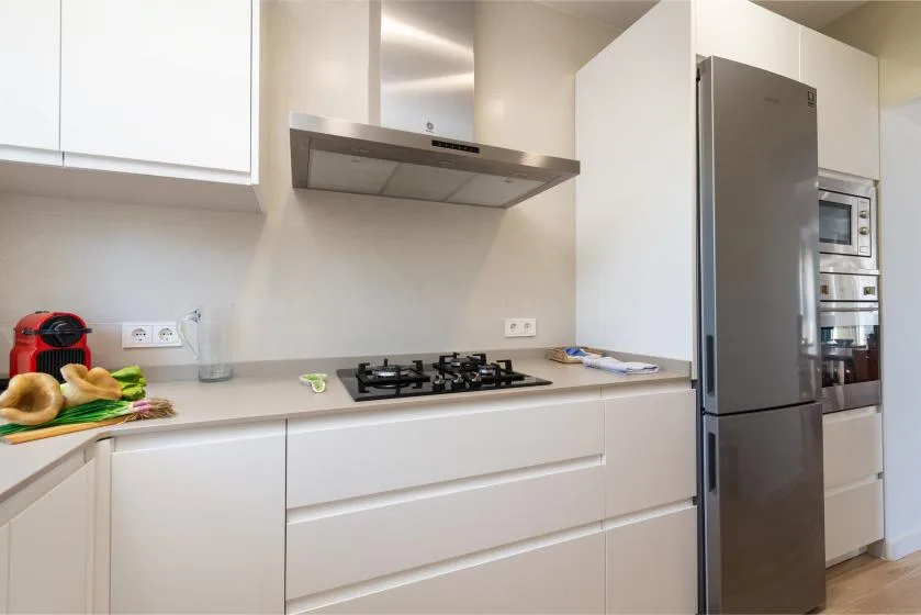 A modern kitchen with a stovetop, range hood, and refrigerator.