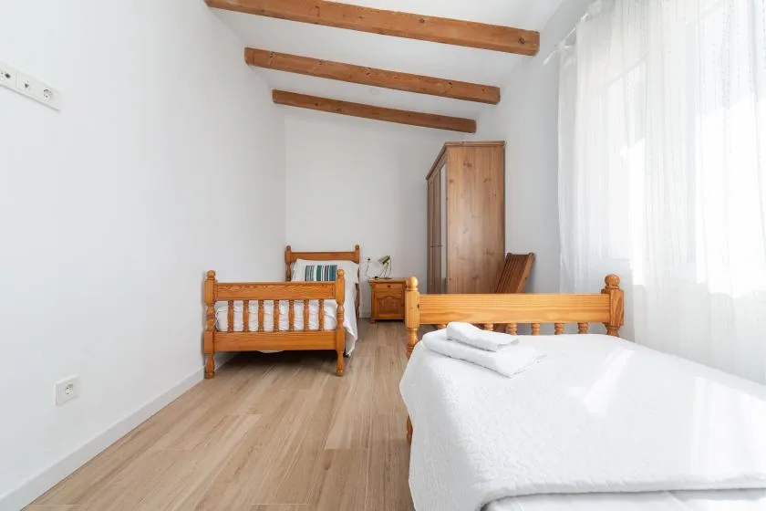 A bright bedroom with wooden beds, a wardrobe, and exposed ceiling beams.