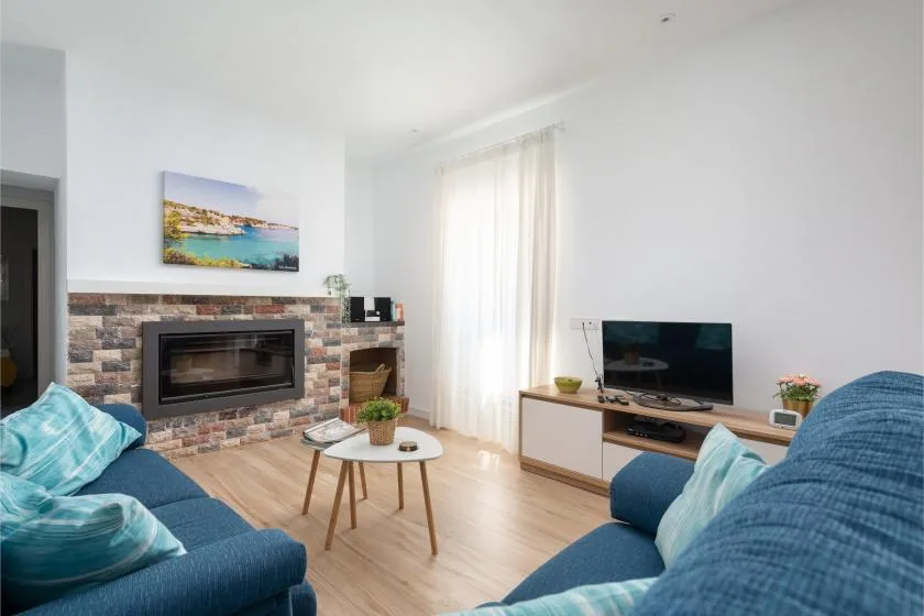 A bright living room with blue seating, a fireplace, and a television.