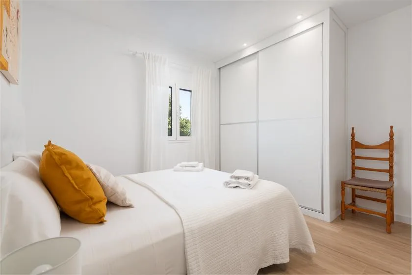 A bright bedroom with a neatly made bed and a large white wardrobe.