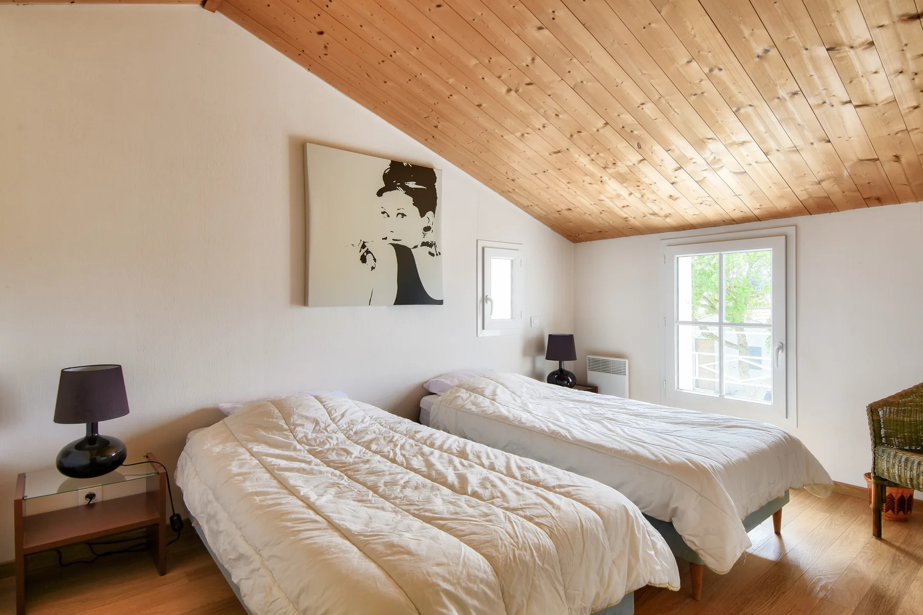 A bright bedroom with two beds and a sloped wooden ceiling.