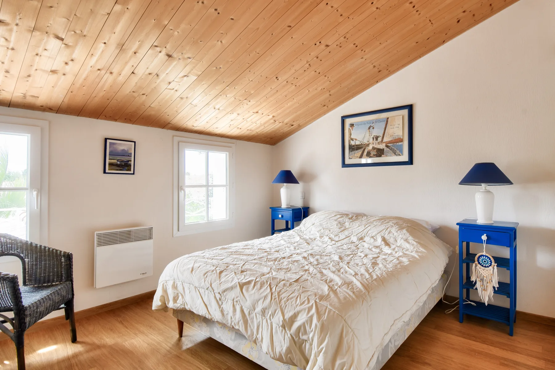A bedroom with a bed, blue bedside tables, and a sloped wooden ceiling.