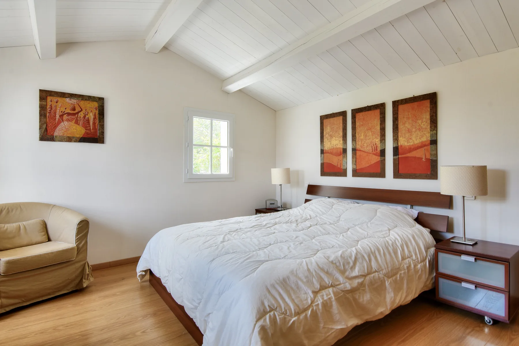 A bright bedroom with a large bed, a window, and framed artwork.
