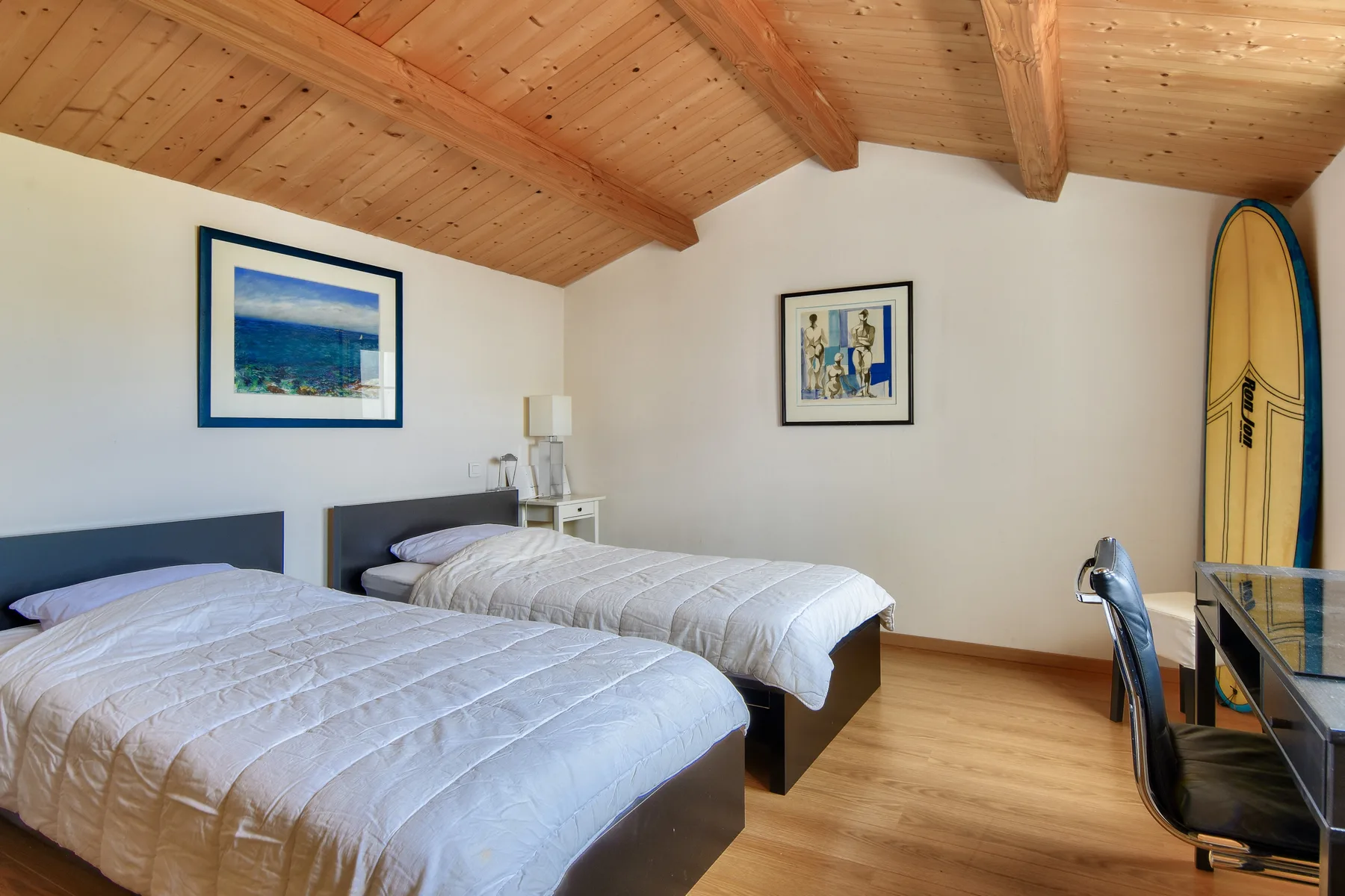 A bedroom with two beds beneath a sloped wooden ceiling.