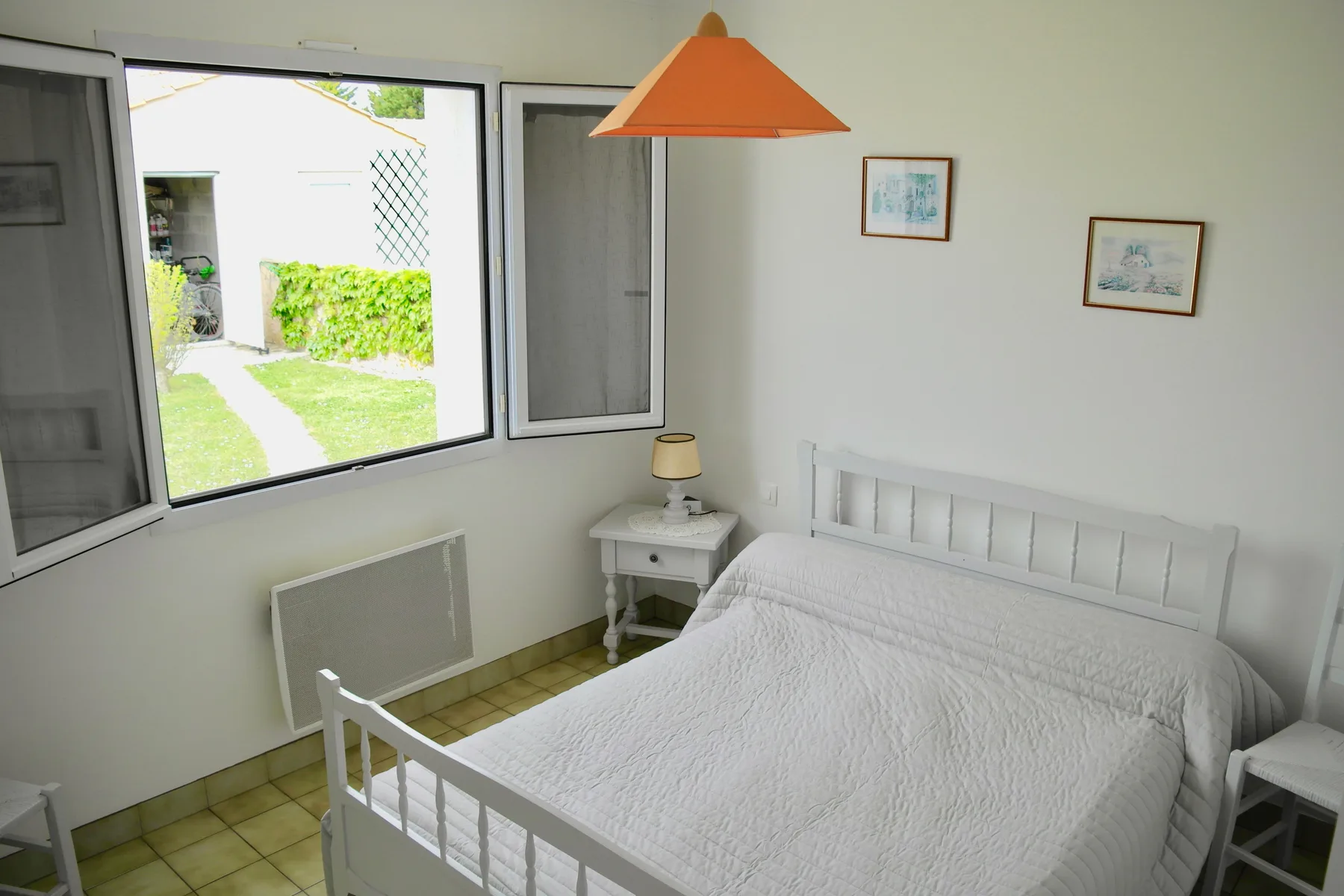 A bedroom with a white bed and a window overlooking a garden.