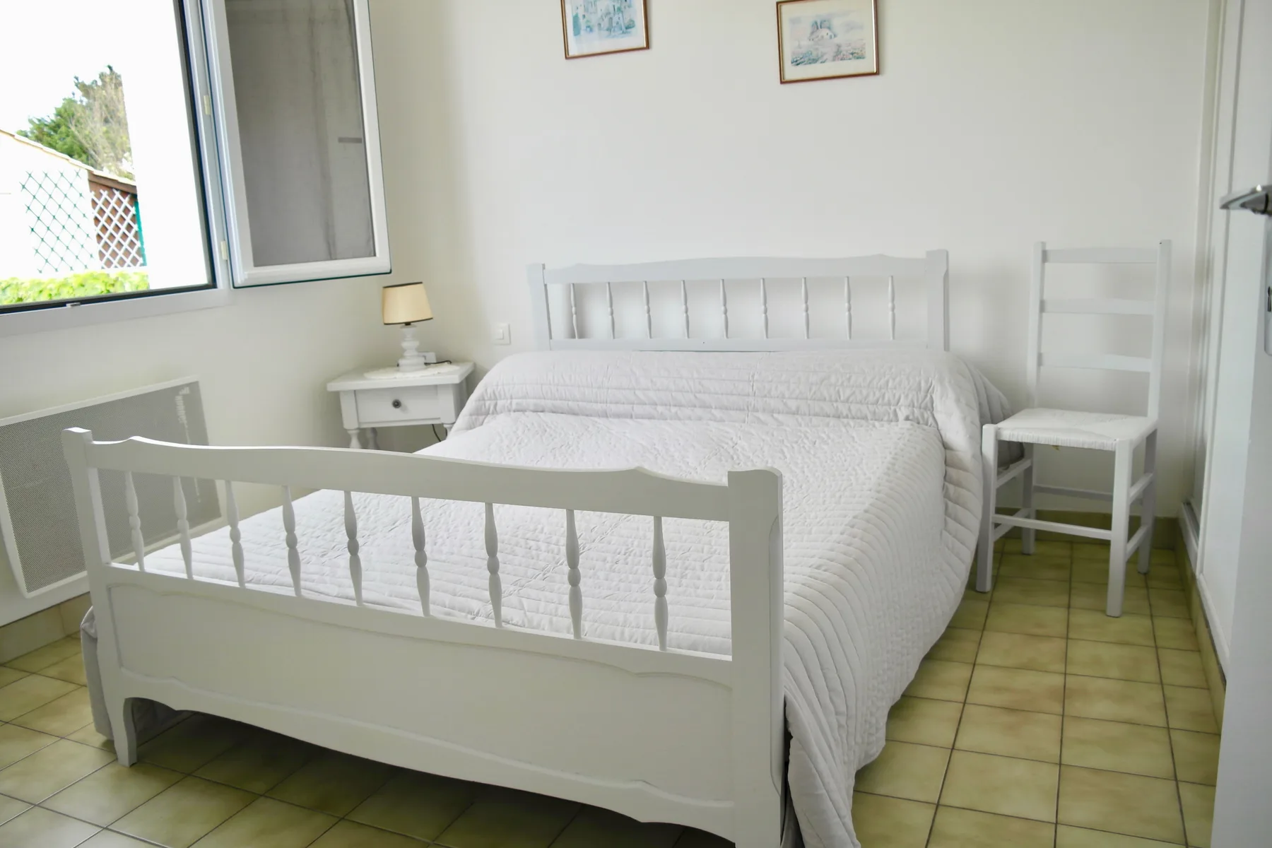 A bright bedroom with a white bed and a bedside table.