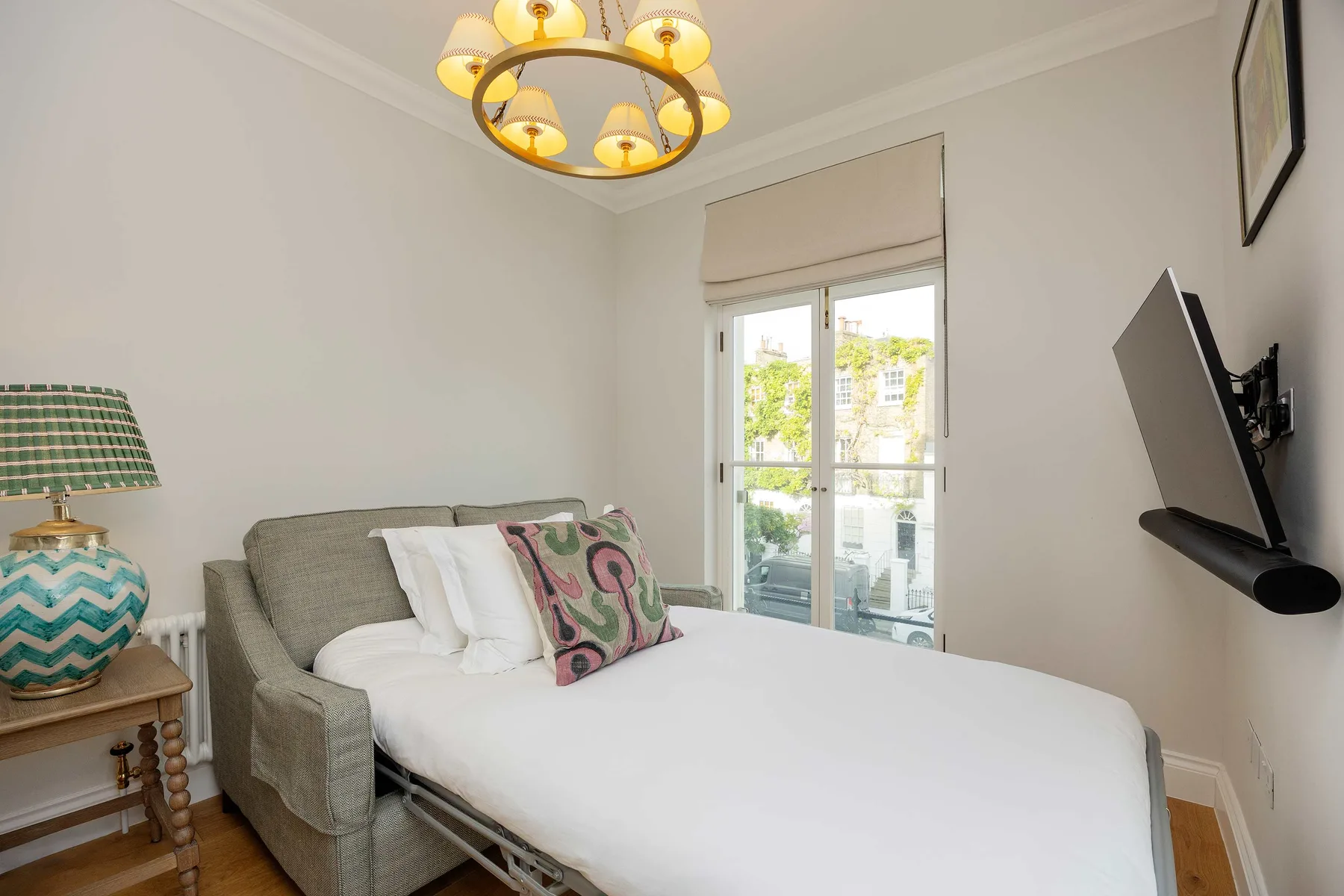 Un dormitorio con una cama bien tendida junto a una puerta de vidrio al balcón.