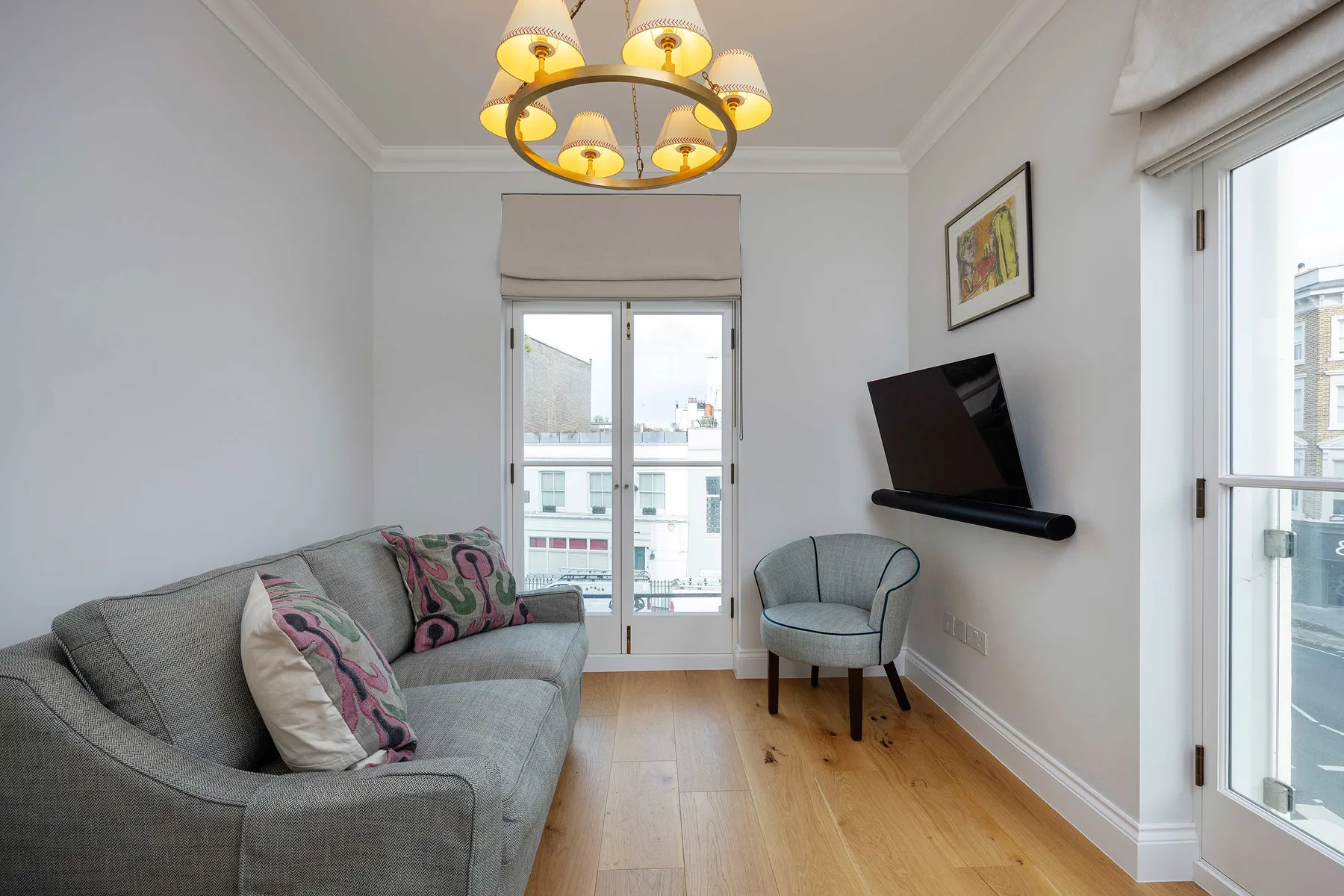 Una sala luminosa con asientos, un televisor en la pared y ventanas grandes.