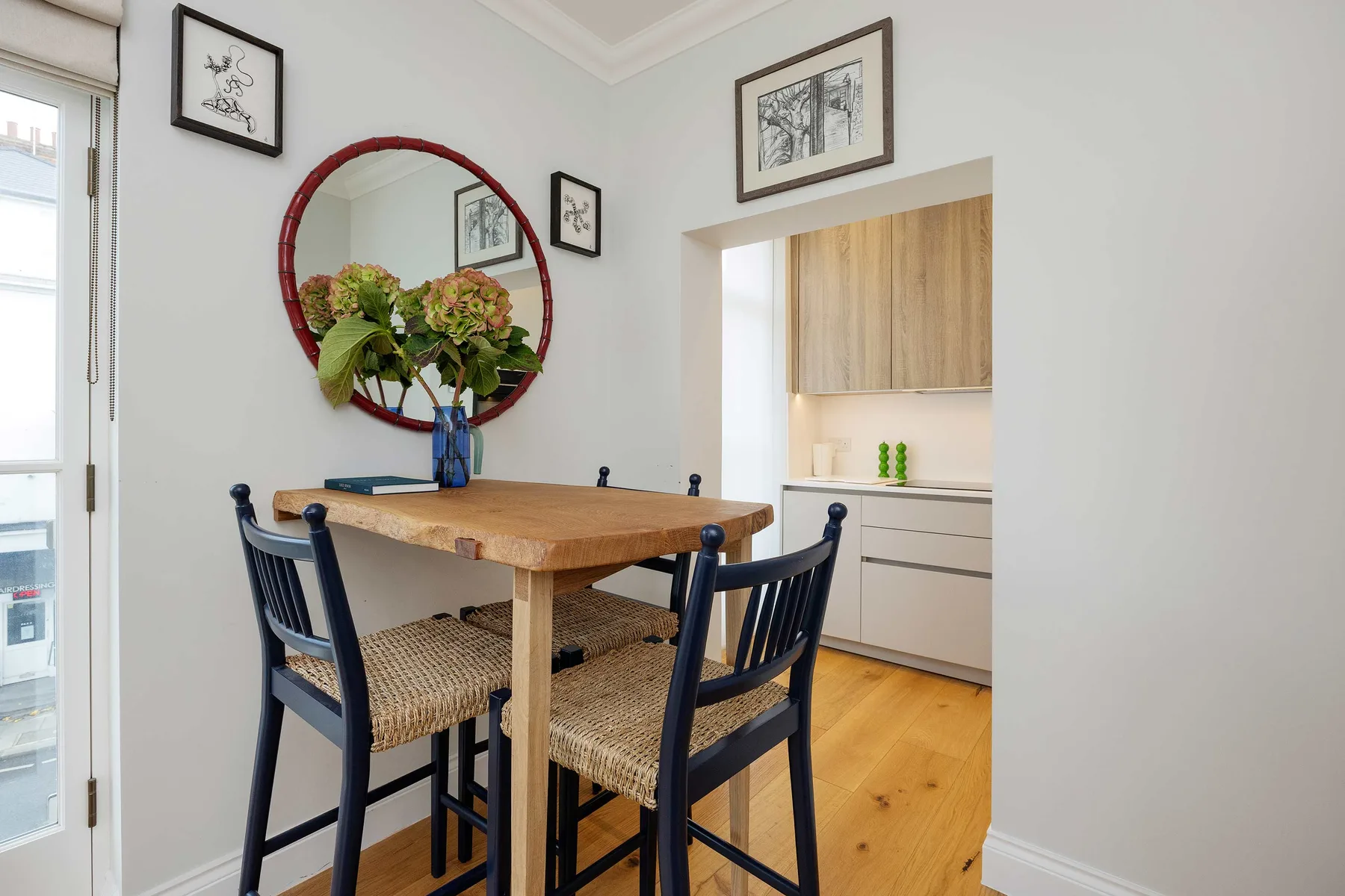 Comedor con una mesa de madera, sillas oscuras y flores en un jarrón.