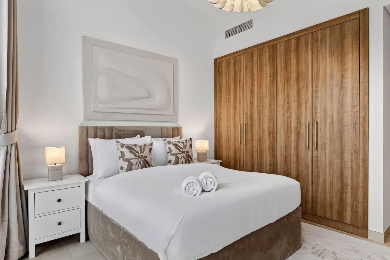 A bedroom with a neatly made bed and a large wooden wardrobe.