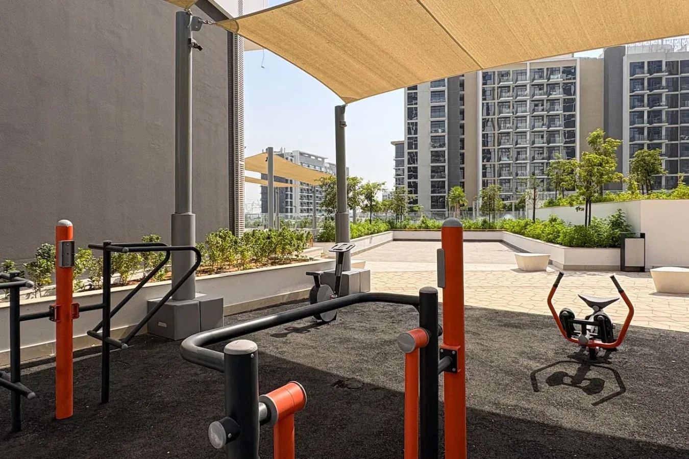 An outdoor fitness area with exercise equipment beneath a shade canopy.
