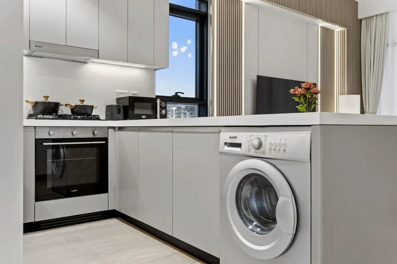 A modern kitchen with white cabinets, an oven, and a washing machine.