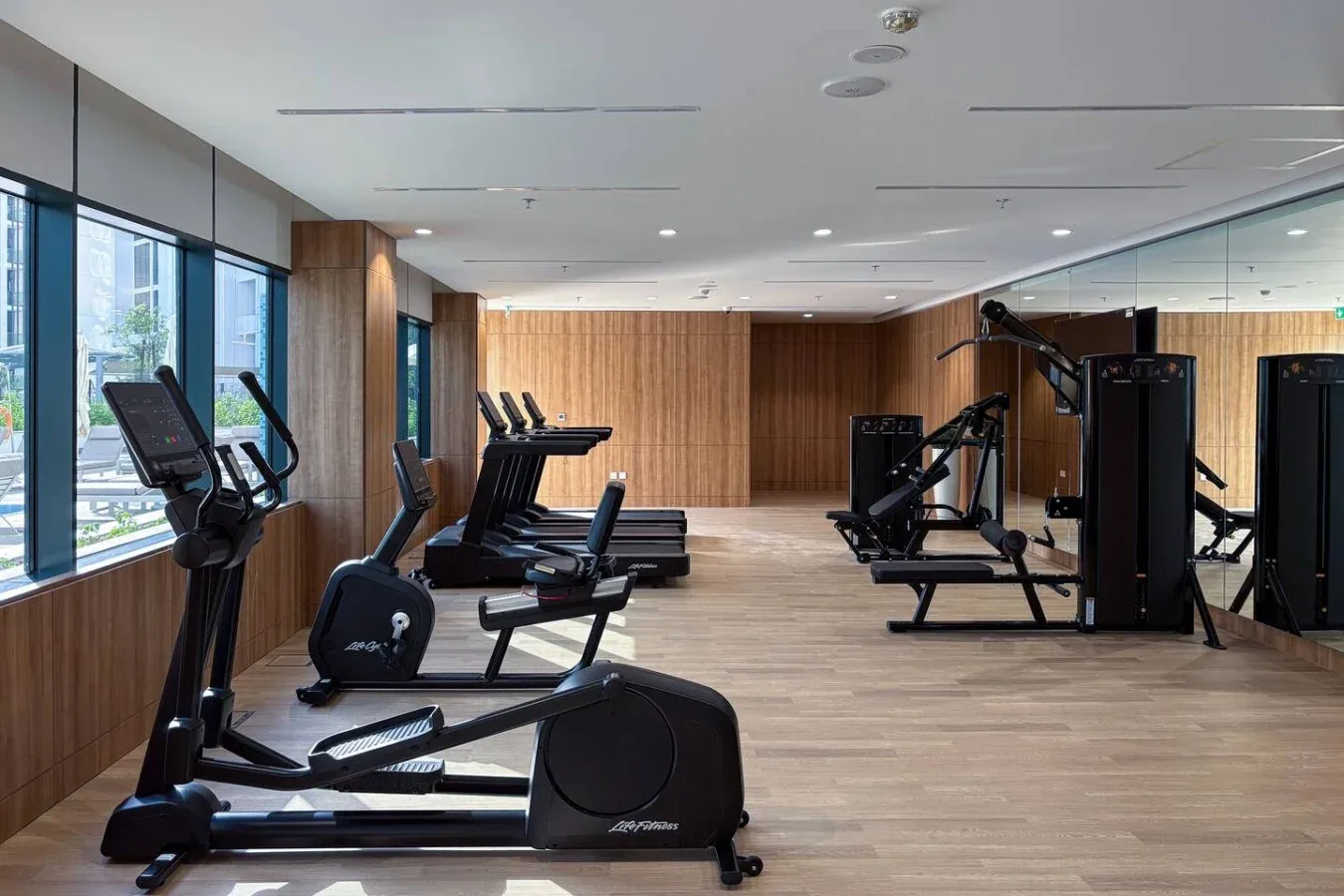 A gym with exercise machines arranged along the windows and mirrored wall.