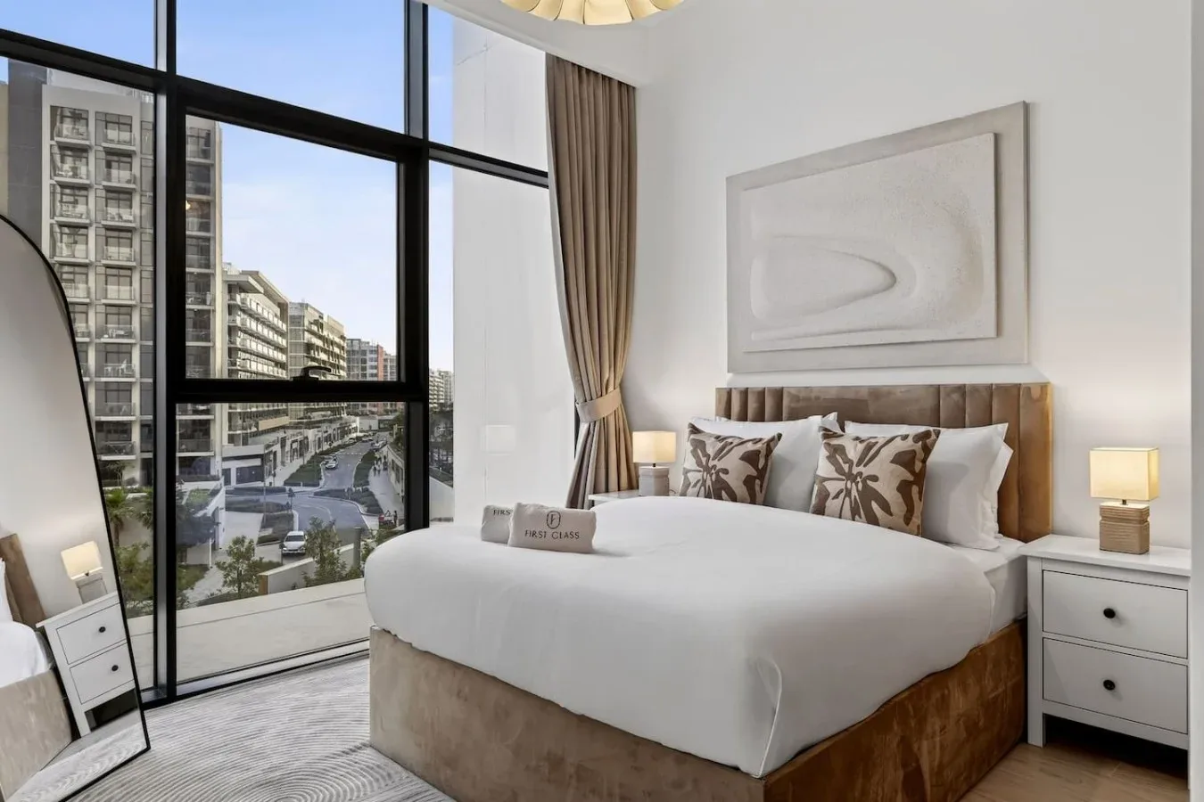 A bright bedroom with a large bed beside floor-to-ceiling windows.