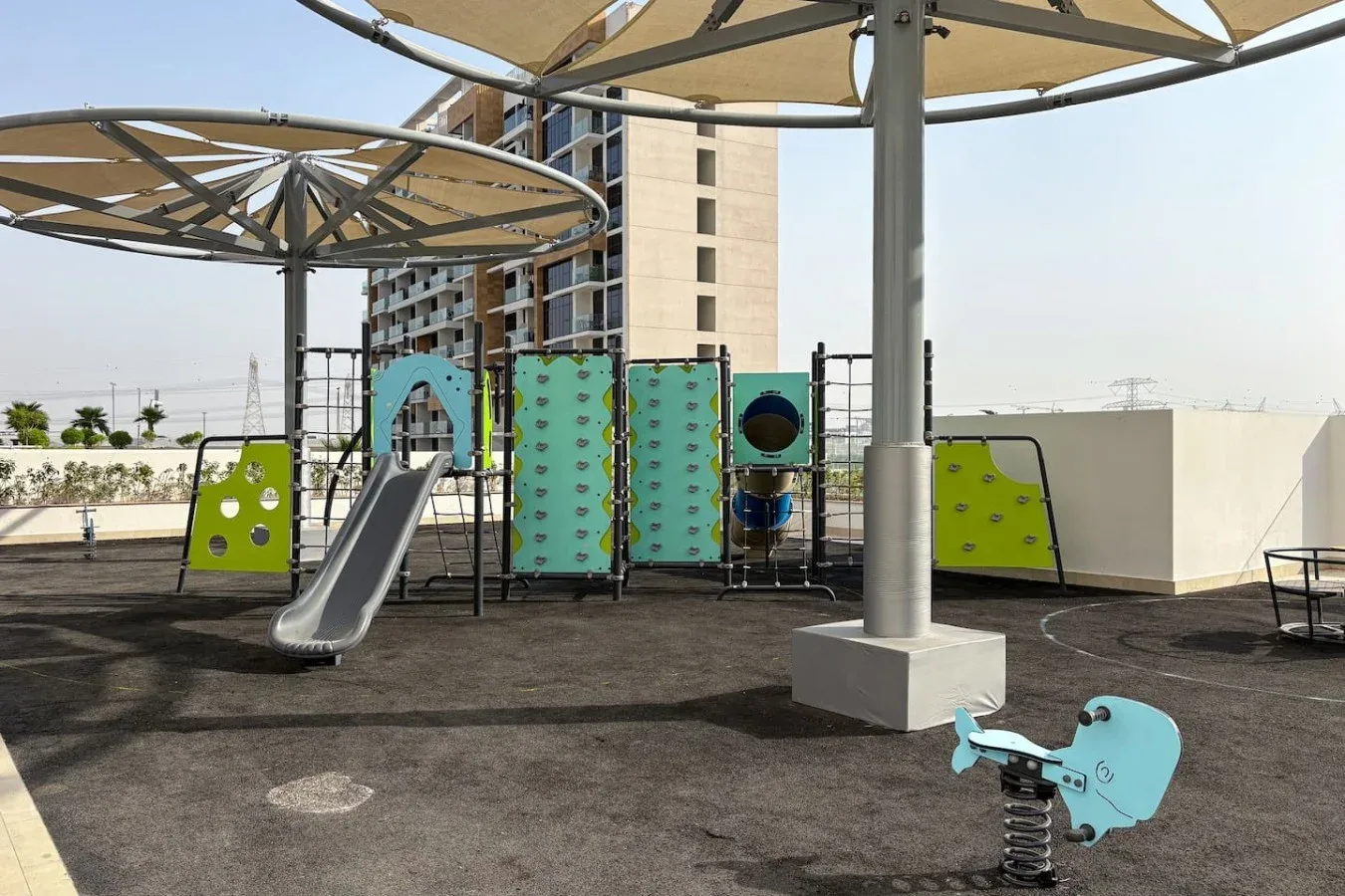 An outdoor playground with climbing panels, a slide, and shade canopies.