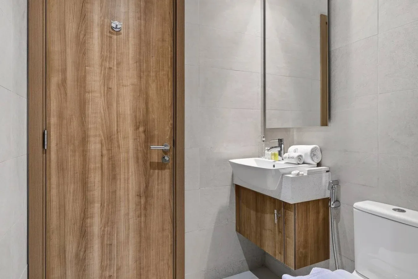A tiled bathroom with a wooden vanity, sink, and mirror beside a wooden door.