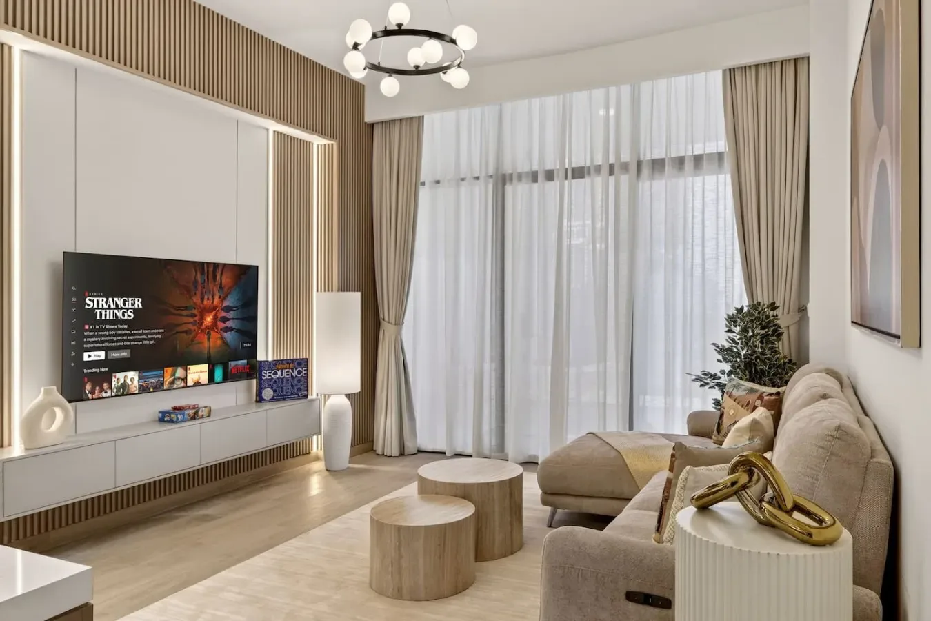 A living room with seating, a television, and tall curtained windows.