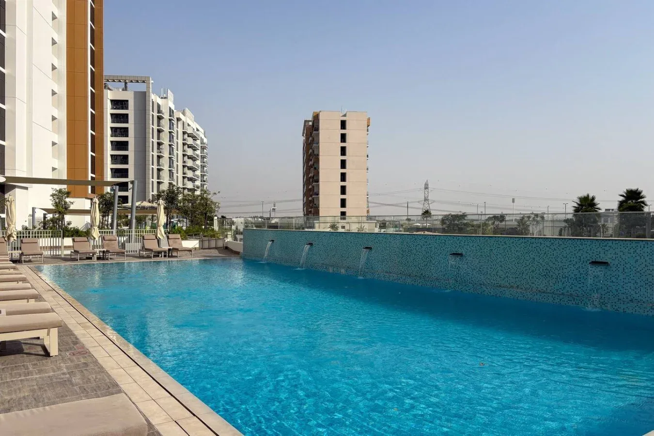 Outdoor swimming pool beside modern apartment buildings, with loungers along the deck.