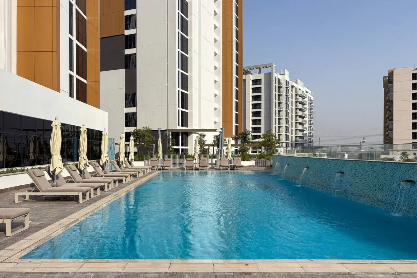 An outdoor swimming pool beside modern high-rise buildings and lounge seating.