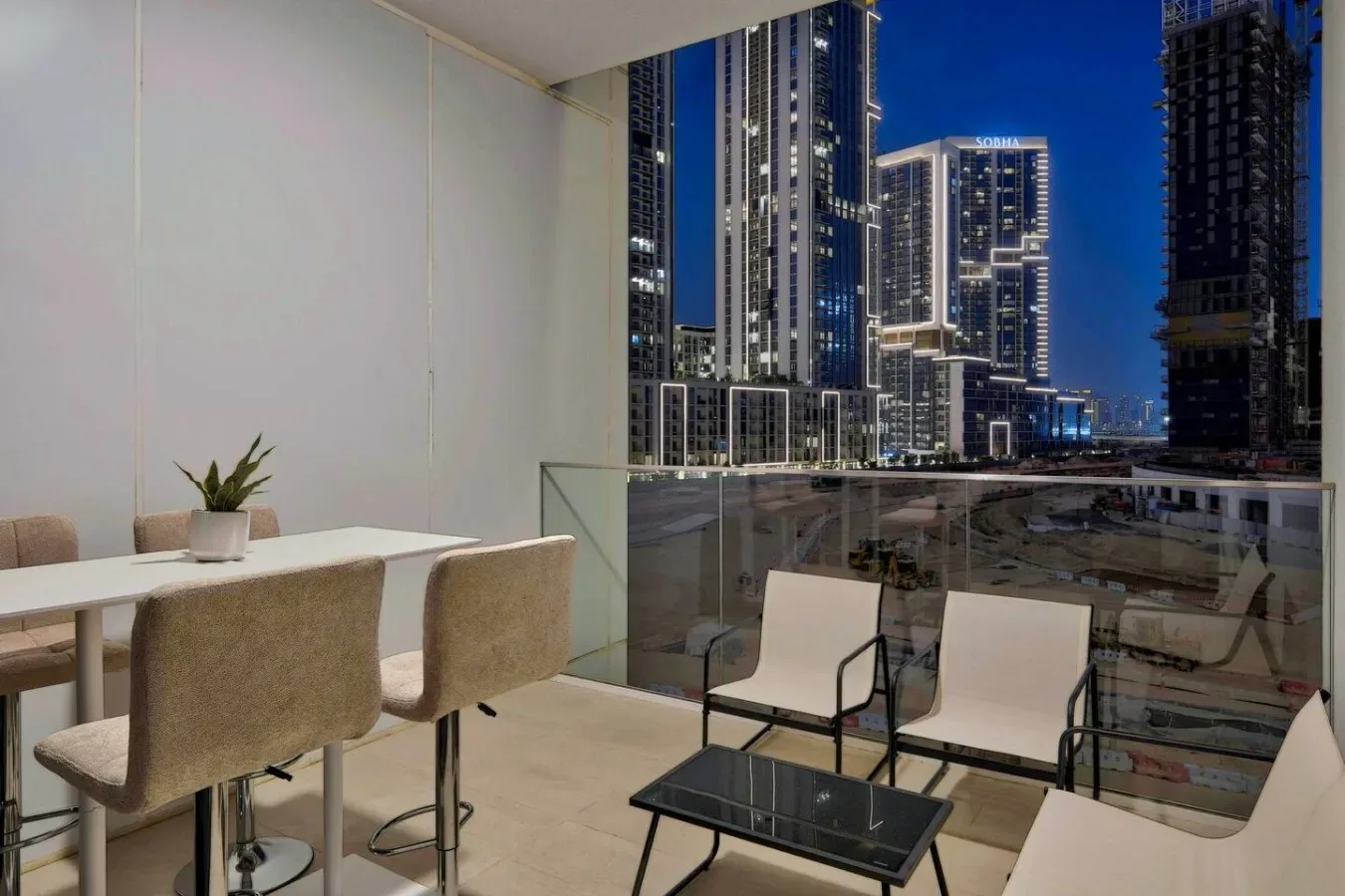 A balcony seating area overlooks illuminated high-rise buildings at night.